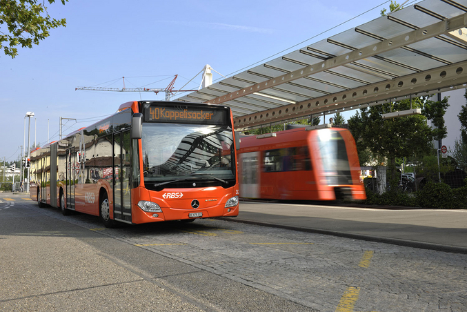 Un autobus rosso della RBS alla stazione Papiermühle di Ittigen con un treno regionale sullo sfondo