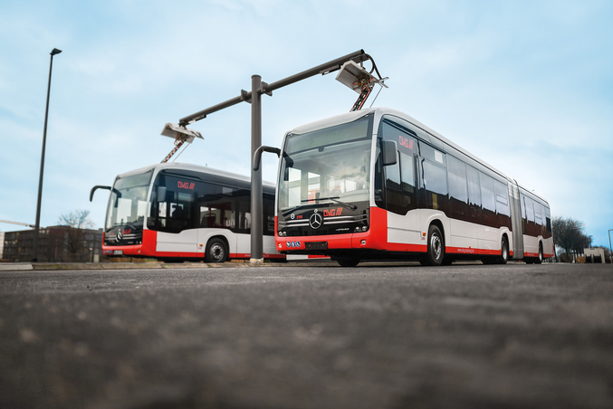 Due autobus elettrici rossi e bianchi di EvoBus vengono caricati in una stazione di ricarica in un deposito.