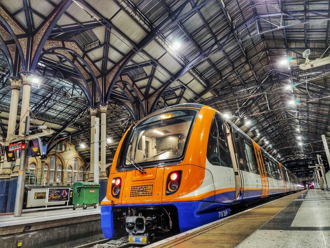 Un treno arancione di Arriva Rail London si trova in una stazione ferroviaria di Londra.