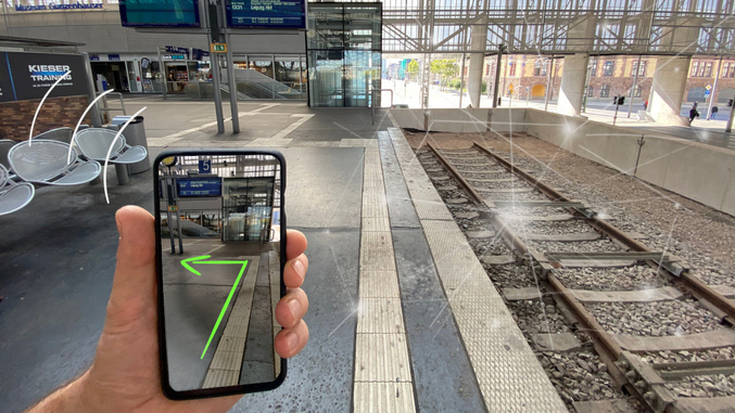 Su un binario ferroviario, una mano tiene uno smartphone che indica un percorso sul binario tramite una freccia.