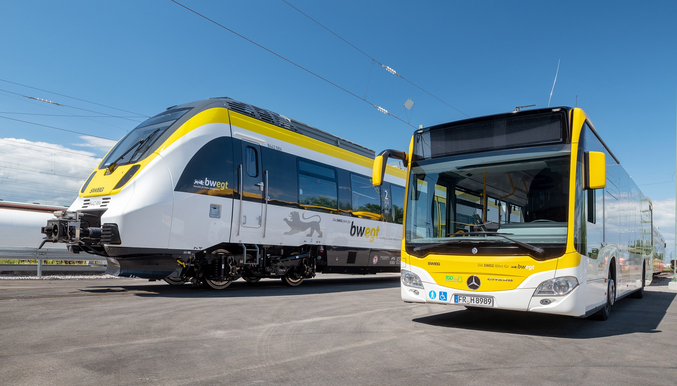 Un autobus giallo e bianco vuoto e un treno SWEG giallo e bianco si trovano uno accanto all'altro in un deposito.