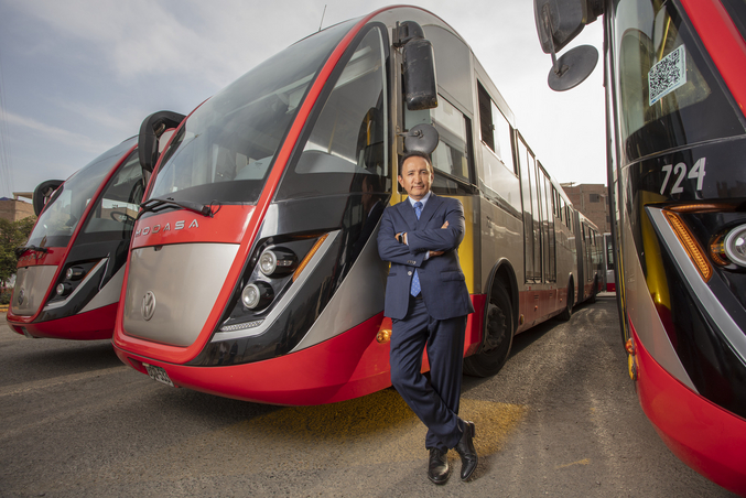 Polo Peréz, amministratore delegato del Grupo Polo, si appoggia a un autobus rosso del Grupo Polo parcheggiato accanto ad altri due autobus rossi in un deposito.