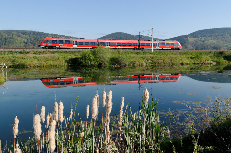 Un treno regionale DB rosso passa un fiume e si specchia in esso.