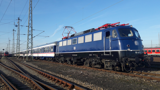 Un treno TRI blu corre da sinistra a destra su binari marroni.