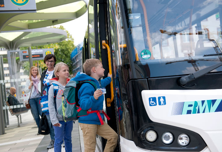 Bambini che accedono a un autobus bianco con il logo RMV sul davanti